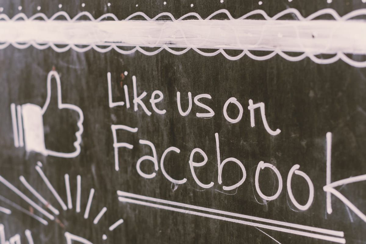 A chalkboard sign with a thumbs-up reading Like us on Facebook