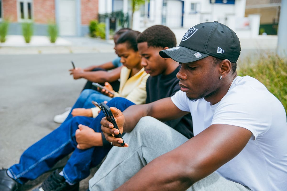 Friends sitting together on a curb, each looking at a phone