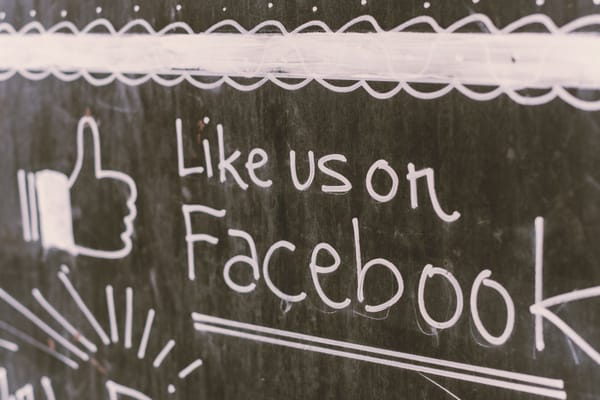 A chalkboard sign with a thumbs-up reading Like us on Facebook