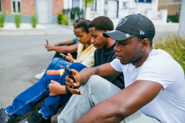 Friends sitting together on a curb, each looking at a phone