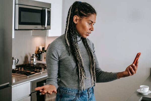 A woman frowning at her phone in the kitchen